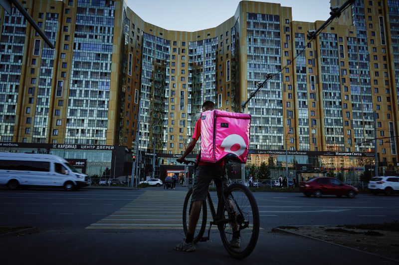 自転車に乗り、ピンクのスクエアバッグを背負った配達員ドライバー